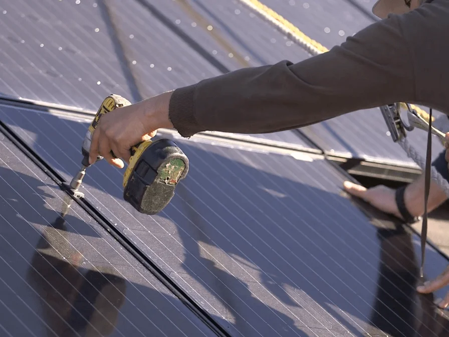 Close-Up Of Auric Solar Workers Securing Solar Panels To Client's Roof