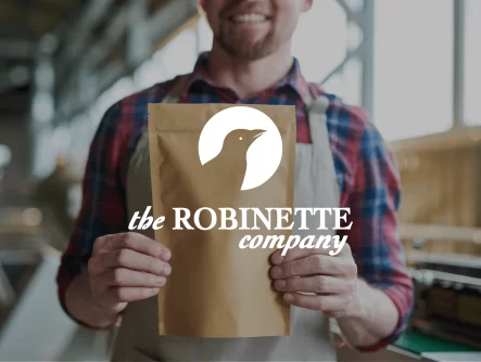 The Robinette Company Logo Overlayed On Picture Of Man Smiling And Holding Paper Packaging
